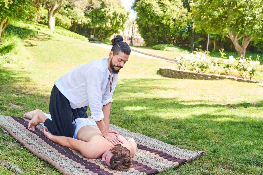 Francisco giving Thai massage to a man laying on a mat on grass